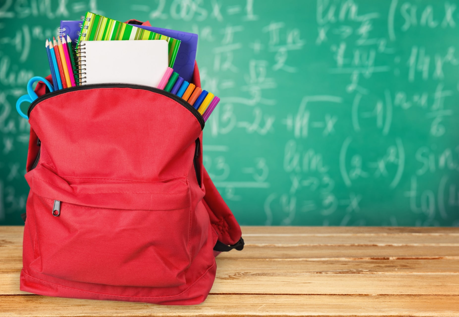 Zaino rosso su banco davanti alla lavagna verse