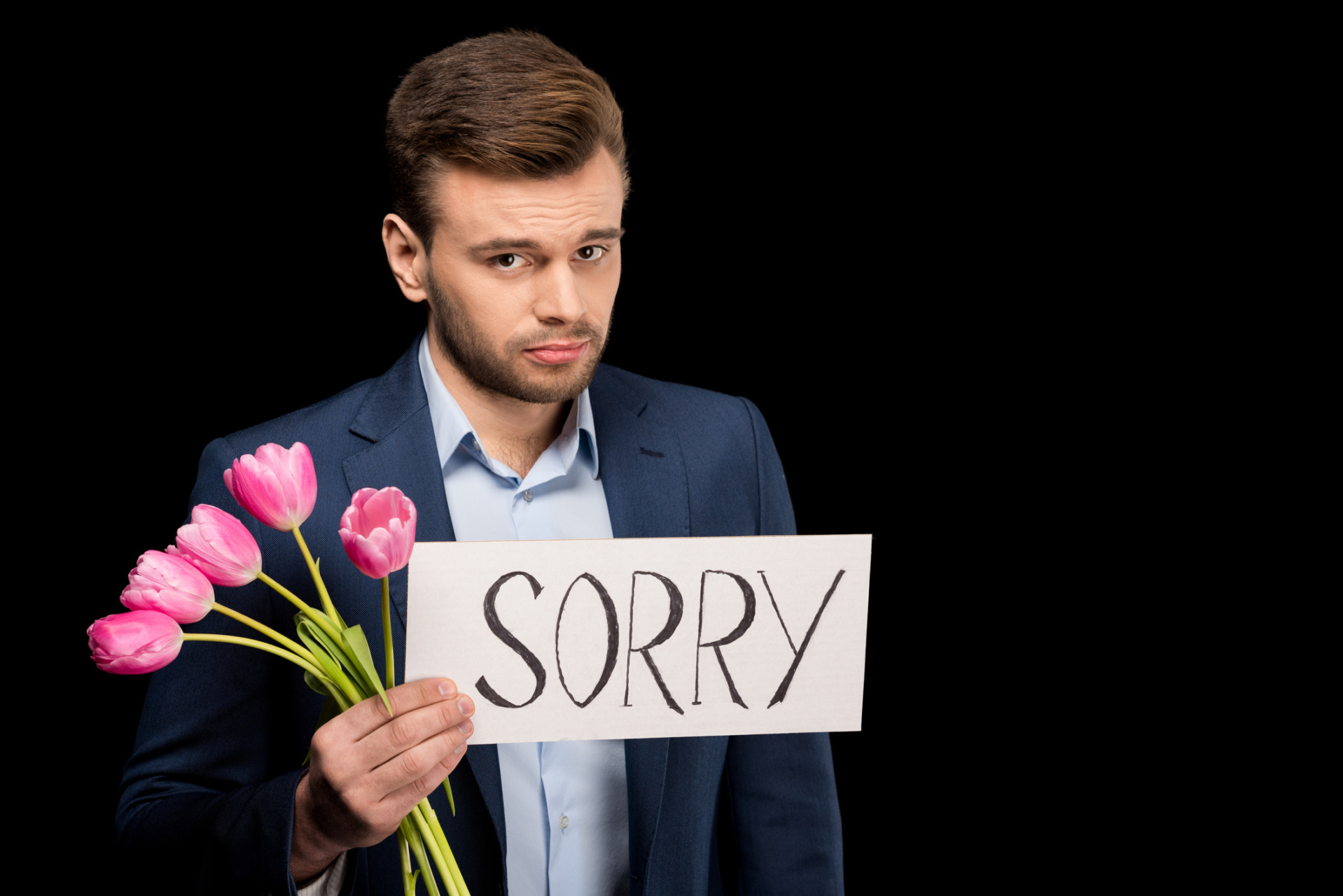 Ashamed young man with tulips and sorry sign looking at camera