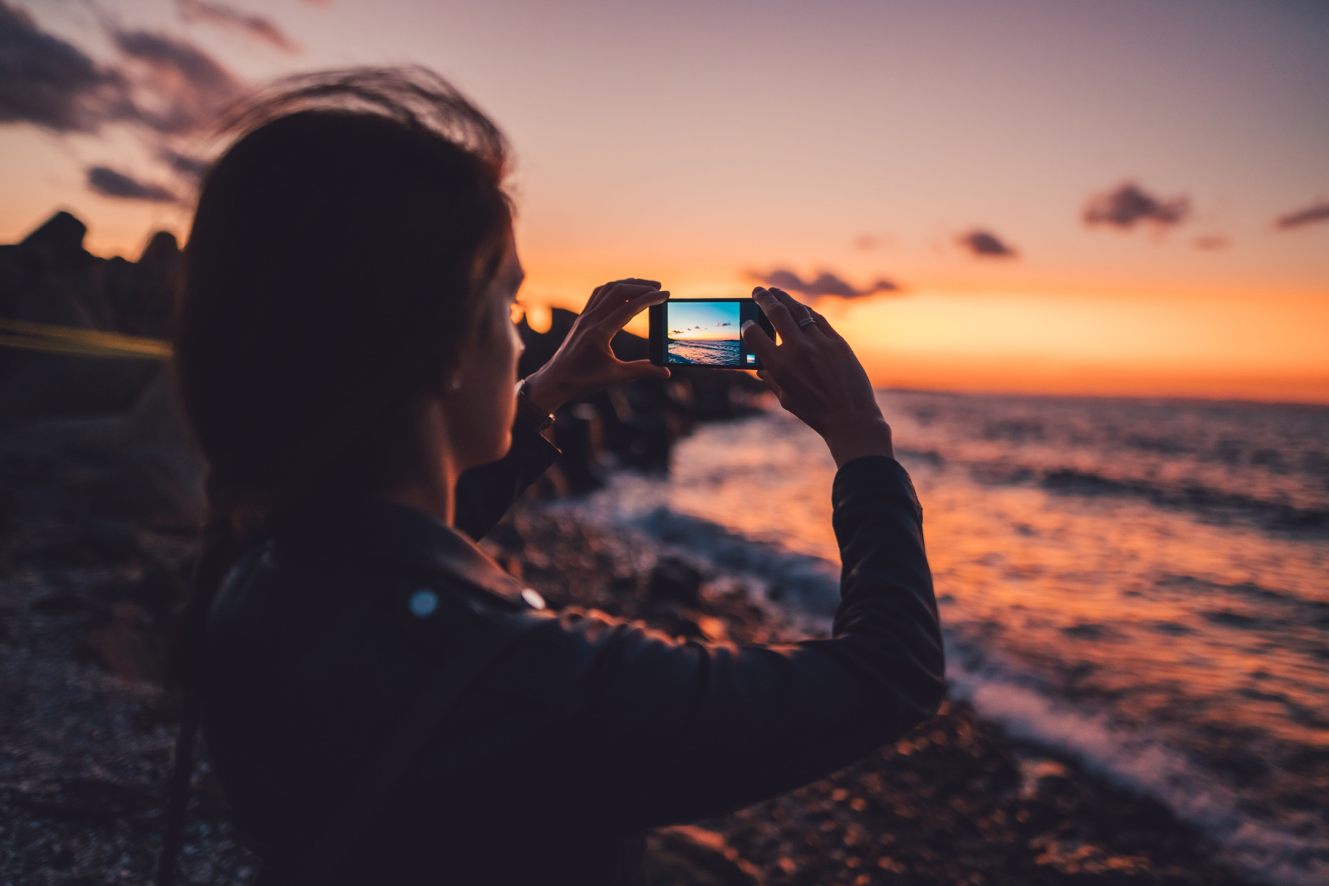 Woman at the beach photographing the sunset