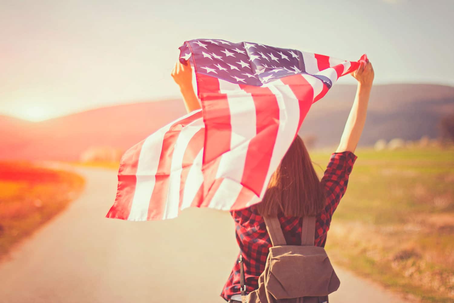 Giovane ragazza con bandiera americana al vento al tramonto