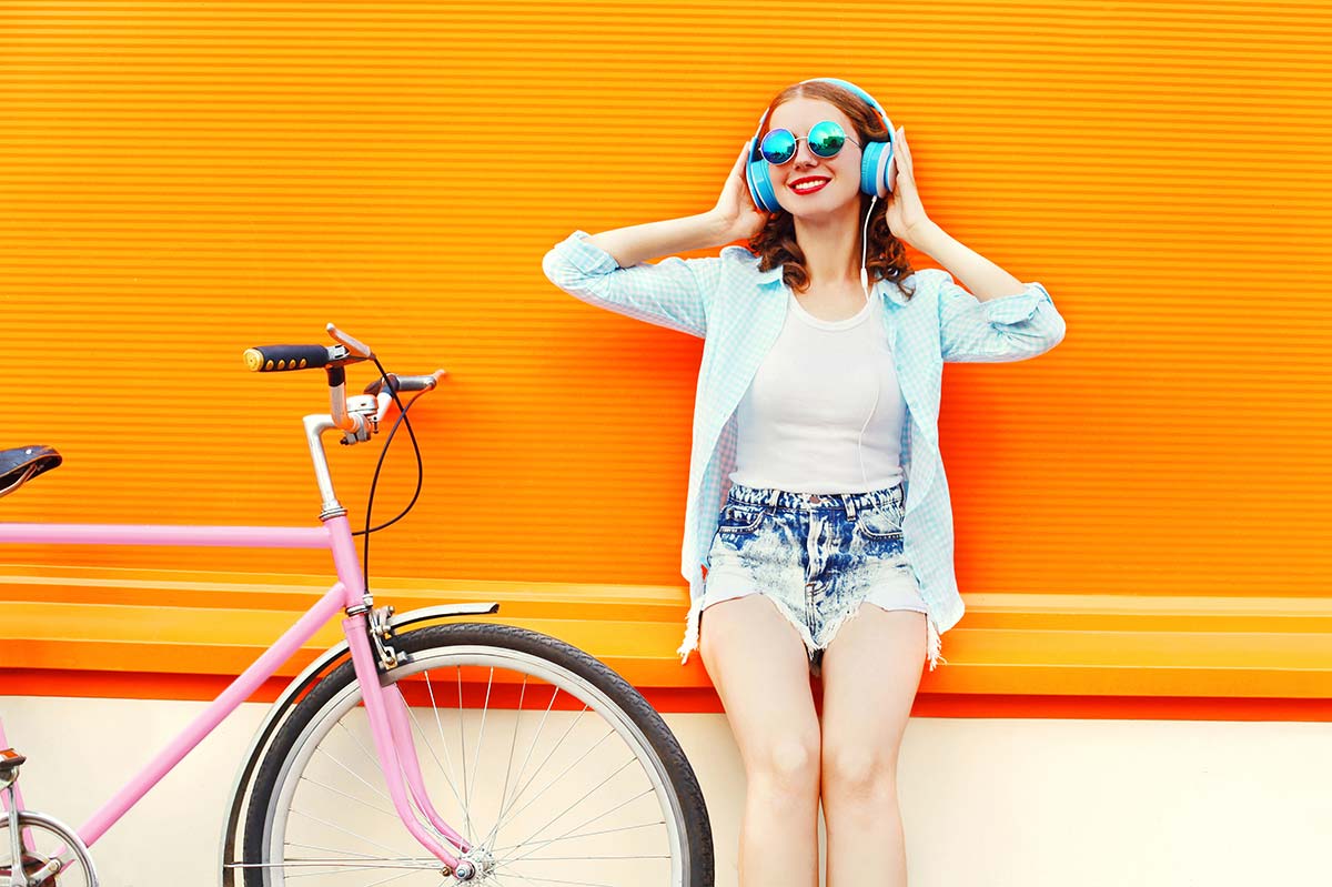 Ragazza che ascolta musica con sfondo arancione e bicicletta