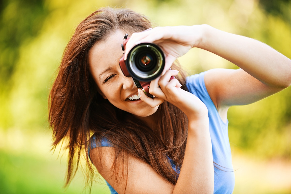 Portrait of beautiful laughing brunette girl wearing blue t-shirt, making photos at summer green park.