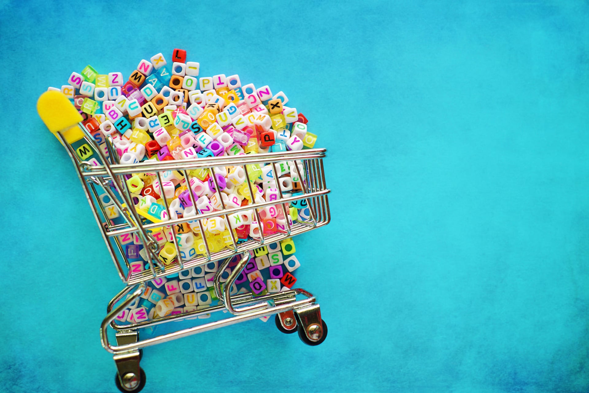 Perchè gli uomini parlano così tante lingue? Mini shopping cart or trolley full of English letter beads on blue background for learning concept, added vintage filter effect