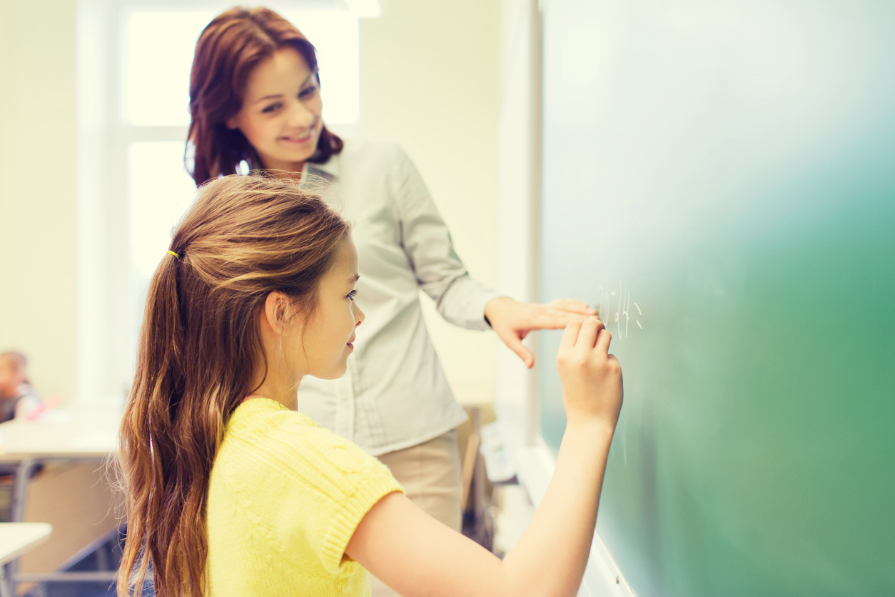 Gli insegnanti italiani lavorano di più e guadagnano di meno Maestra che aiuta l'allieva alla lavagna