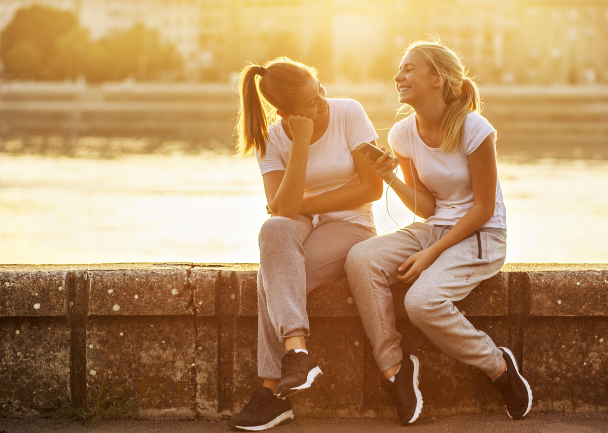 Come migliorare la pronuncia Due amiche sedute su un muretto che ridono con lo smartphone in mano