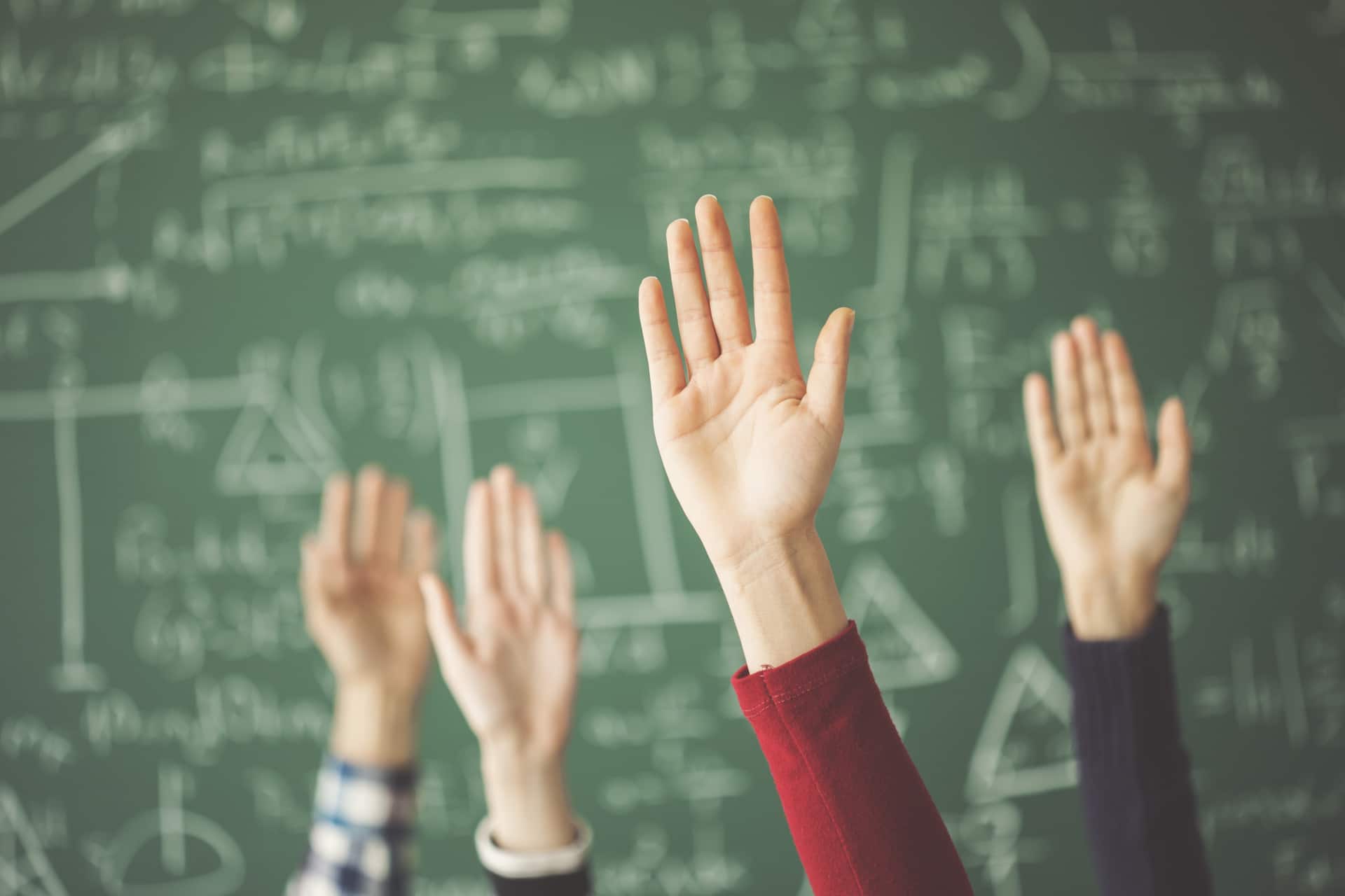 Come un insegnante può cambiare la vita dei suoi studenti Students raised up hands green chalk board in classroom