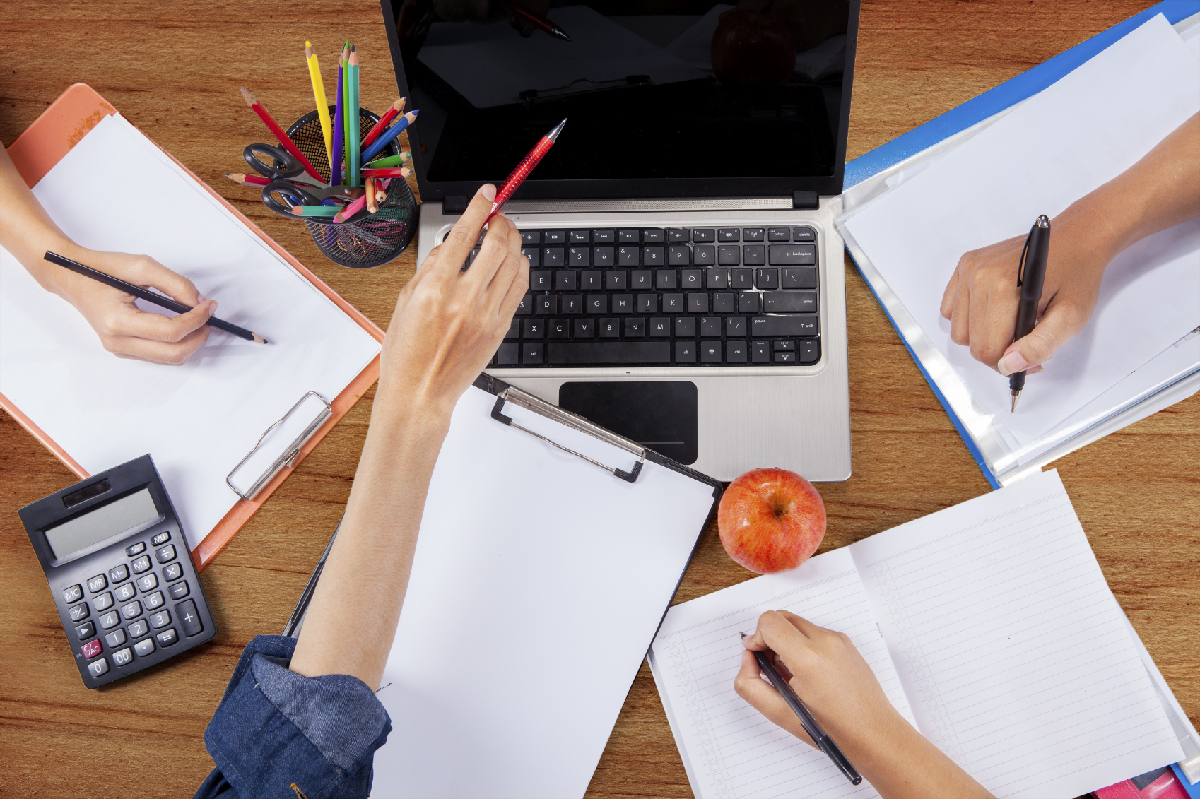 Le WEBQUESTS nella didattica dell’inglese tavolo ripreso dall'alto con mani che scrivono su bloc note e indicano un pc